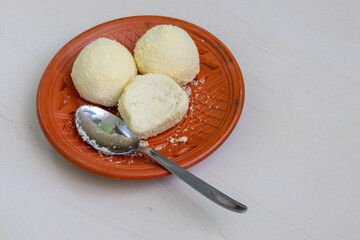 Tasty Kachagolla sweets and a spoon, served on a clay plate, rest on a light wooden surface. It is a popular Bengali sweet known for its soft, spongy texture and subtle sweetness.