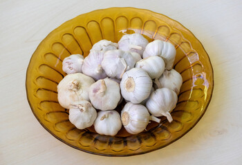 Fresh garlic in a glass plate on a wooden surface.