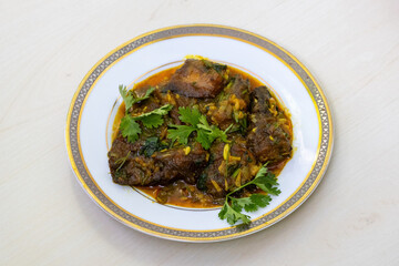 A flavorful shing fish bhuna curry, served elegantly on a white plate and adorned with a sprinkling of fresh coriander leaves.