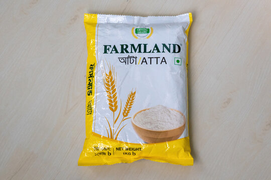 A packet of Farmland Atta wheat flour on a wooden background. Farmland Atta is a popular brand in Bangladesh known for its high quality and consistent taste.