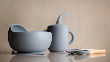 Silicone baby tableware set in gray, the first soft cup for toddlers. Baby eating utensils. Nutrition and feeding concept
