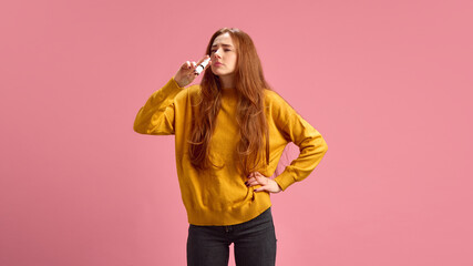 Young redhaired woman in orange sweater using nasal spray for allergy relief, trying to alleviate...