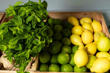 fresh peppermint, lemons and limes in wooden box in grocery store or supermarket. Juicy ingredients for mojito long drink. Summer fruit for lemonade or desserts