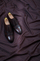 Male classic formal dark brown leather shoes on fabric suit background. Copy space for logo design, advertising. Natural leather accessories for men