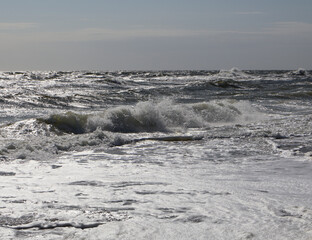 Waves crashing on shoreline with white foam under a cloudy sky. Coastal seascape photography. Nature and ocean concept for design and print.