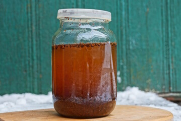one large glass jar full of brown tea drink and closed with a lid stands on a wooden table near a green wall