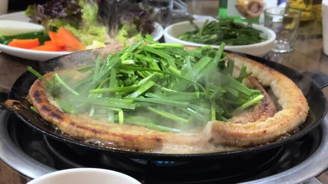 뜨거운 불판 위에 둘둘 말려 올라간 소곱창이 부추와 함께 지글지글 구워지며 곱창에서 나온 맛있는 육즙이 흐르는 모습
