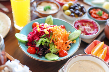 Delicious rich Traditional Turkish breakfast include tomatoes, cucumbers, cheese, butter, eggs, honey, bread, bagels, olives and tea cups.