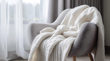 A cozy grey armchair draped in a white cashmere blanket. Highlight the luxurious feel and calming atmosphere of the monochromatic tones.