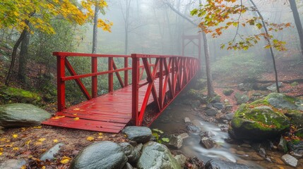 Red suspension bridge shrouded in mist surrounded by vibrant autumn foliage and rocky streams in a tranquil forest setting.
