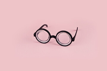 Minimalistic round black glasses with placed on pastel pink background, perfect for playful or creative themes with copy space