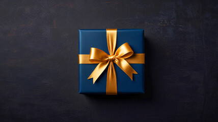A dark blue gift box with a gold ribbon placed on a dark background. The gift box has a festive concept, perfect for a birthday, There is ample copy space around the gift box.