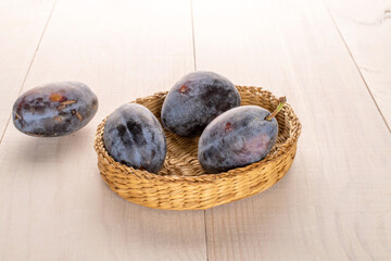 Black ripe plums with household utensils on a wooden table, close-up.