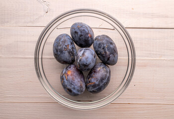 Black ripe plums with household utensils on a wooden table, close-up, top view.
