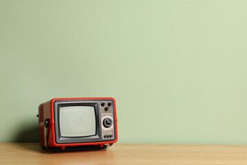 Obraz premium Retro tv set on wooden shelf against green wall. Space for text