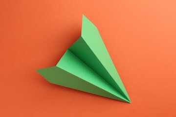 One handmade green paper plane on orange background, top view