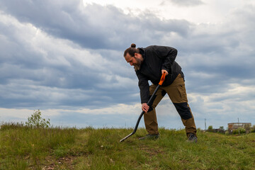 A man is digging in the grass with a metal shovel