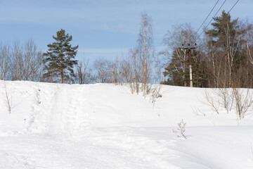 Fototapeta premium Snowy path leading uphill, bare trees and a clear blue sky create a serene winter landscape