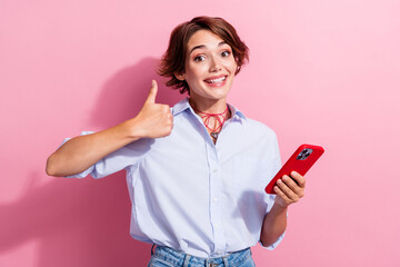 Portrait of charming girl wear blue stylish blouse hold smartphone showing thumb up toothy smiling isolated on pink color background