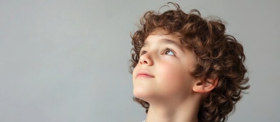 Thoughtful boy with curly brown hair looking up against a neutral background with ample copy space for text or design elements