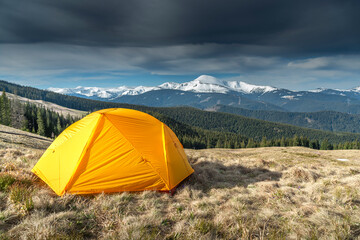 Tent on Foreground In The Mountains, First Morning Light. Campsite with a yellow dome tent on a high mountain bluff on the background of snowy mountains at sunrise.Travel concept. © XArt