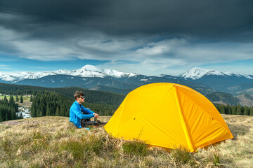 Man Sitting Outside of His Tent at Sunrise. Hiker prepares hot coffee in alpine campsite in the morning.