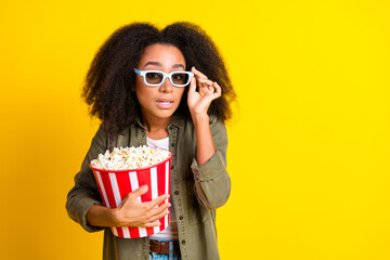 Obraz premium Photo of focused girl with perming coiffure wear khaki shirt in 3d glasses hold popcorn touch glasses isolated on yellow color background
