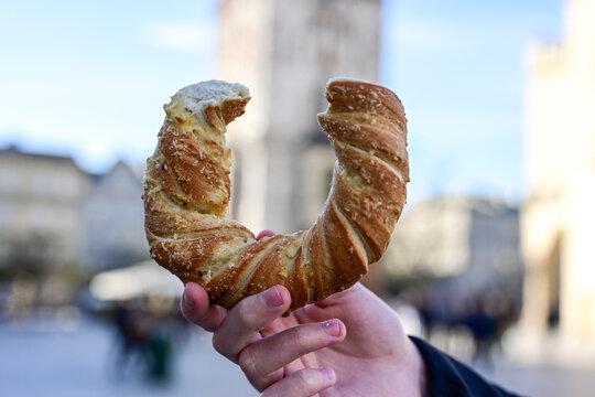 Hand holding obwarzanek krakowski prezel on Cracow Main Market Square. St. Mary's Basilica, Bazylika Mariacka Krak&oacute;w or Kości&oacute;ł Mariacki 
