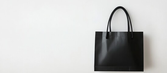 Elegant black shopping bag on minimalist white background with blank space for branding or promotional text.