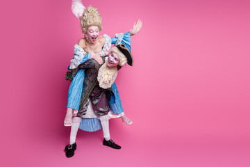 Elegant couple dressed in period costumes enjoying a playful moment against a vibrant pink background at a themed party