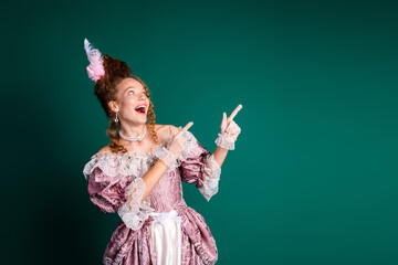 Joyful woman in elegant baroque costume pointing playfully with a modern green background