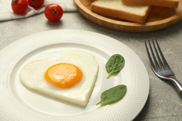 Heart shaped fried egg served on grey marble table, closeup