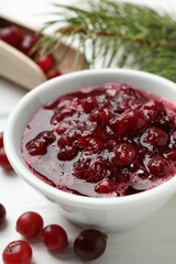 Tasty cranberry sauce in bowl and berries on white table, closeup