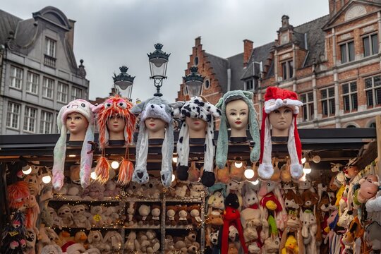 Funnt display of hats on mannequin heads for sale at Christmas market, Bruges, Belgium. Typical stepped gabbles buildings facades.