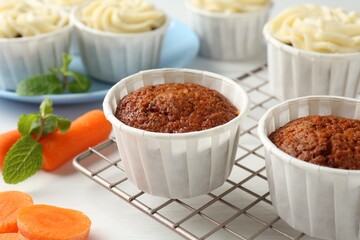 Delicious carrot muffins and fresh vegetables on white wooden table, closeup