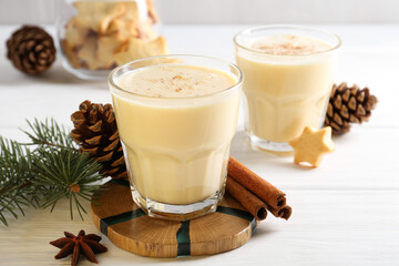 Tasty Christmas cocktail (eggnog) in glasses, pine cones and spices on white wooden table, closeup