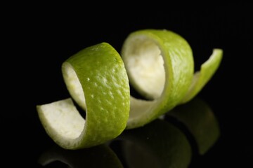 One curly lime peel on black mirror surface, closeup