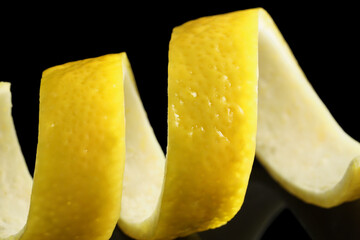 One curly lemon peel on black mirror surface, macro view