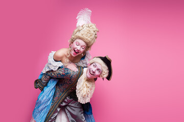 A couple dressed in elaborate vintage costumes poses against a vibrant pink background, embodying the elegance and glamour of a bygone era