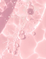 Closeup of splashes and bubbles pink transparent clear calm water surface texture. Trendy abstract summer nature background. Coral colored waves in sunlight. pink cosmetic toner