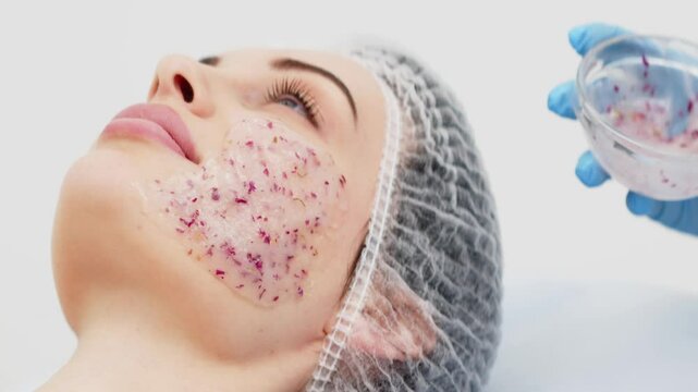 Close-up of a cosmetologist&rsquo;s hands applying an alginate mask with rose petals to a young woman&rsquo;s face in a professional beauty salon. Concept of skincare and relaxation in spa treatments.