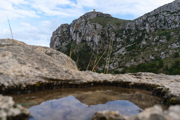 Cap de Formentor, Mallorca, Spain 25.10.2021 - Talaia d'Albercutx watchtower reflected in natural water pool with mountain backdrop