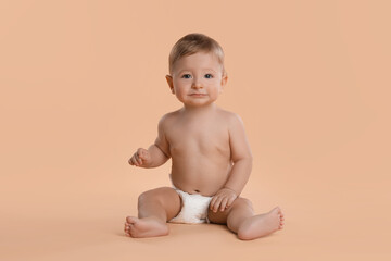 Cute little baby in diaper sitting on beige background