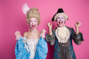 Young couple dressed in baroque costumes enjoying a fun moment, set against a bright pink background.