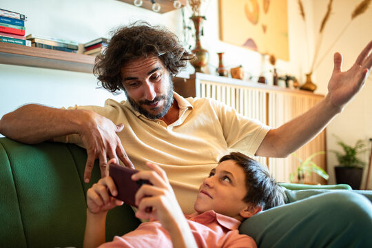 Father bonding with son on couch while discussing smartphone game