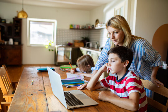 Mother helping kids with online homework at kitchen table