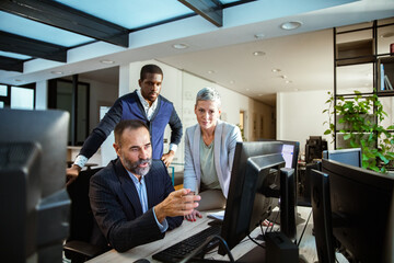 Team collaboration at office desk with dual monitors and brainstorming