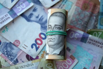Roll of 500 Ukrainian Hryvnia money bills lies on big pile of ukrainian currency money close up
