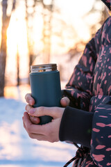 Thermos with hot drink and steam held by hand in winter in sunset light.