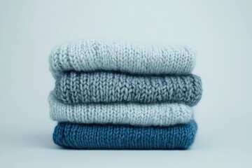 Stack of four knitted sweaters in varying shades of blue, showcasing texture and warmth.